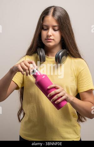 A young woman holds and opens a reusable, eco-friendly pink water bottle, promoting a healthy and sustainable lifestyle. Stock Photo