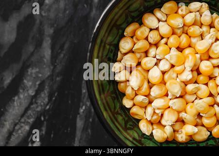 Yellow popcorn kernels in green bowl. Raw corn seeds on dark background. Ingredient for popping. Natural snack close-up. Unpopped corn texture. Stock Photo