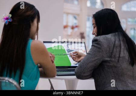 Two women collaborate on a presentation, sharing ideas and refining business strategies. Using a laptop, they focus on project development and innovat Stock Photo
