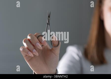 Manicure master's hand with scissors performing perfect beige manicure, salon close-up Stock Photo