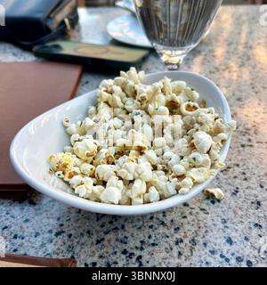 A modern white, boat-shaped bowl holds a generous serving of freshly popped, seasoned popcorn, lightly sprinkled with finely chopped green herbs, like Stock Photo