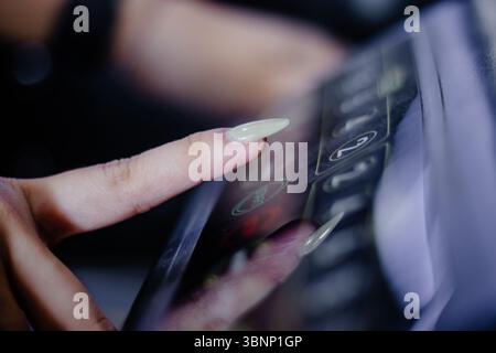 A close-up shows a woman's finger with elegant nails pressing a button on an elevator panel. The image captures the essence of vertical transportation Stock Photo