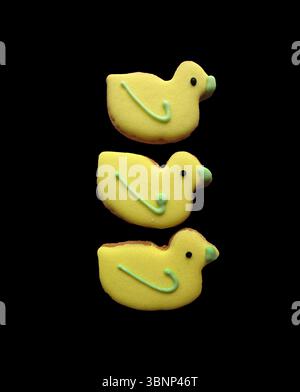 Three yellow duck-shaped biscuits isolated on a black background. Stock Photo