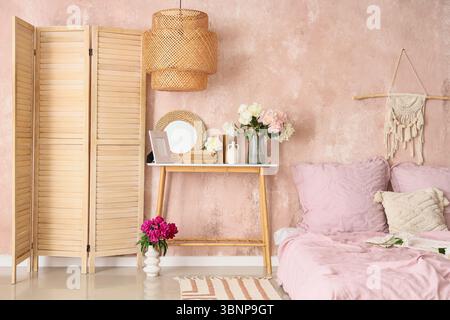 Bedside table with mirror, books and beautiful peonies in bedroom Stock Photo
