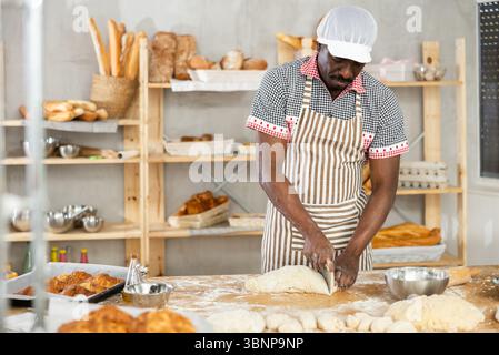 Focused black baker slicing dough in artisan bakery Stock Photo
