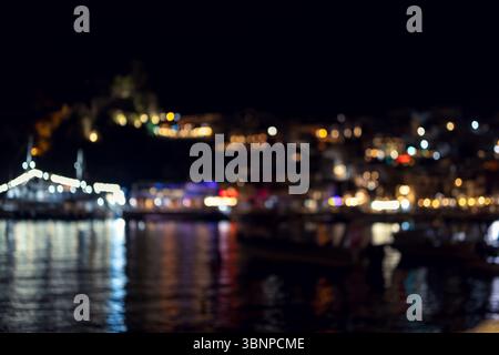 an intentionally blurred photograph capturing the nighttime ambiance of a harbor. the city lights lining the waterfront and reflecting on the dark wat Stock Photo