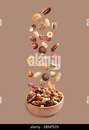 Peanut and other nuts falling into bowl on color background Stock Photo