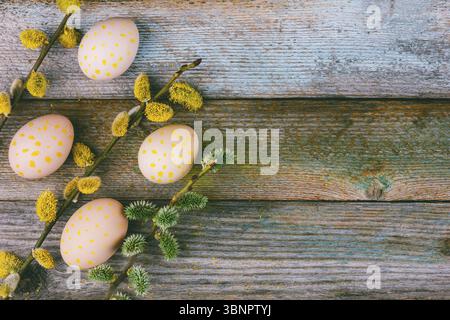 Easter composition of blooming willow twigs and Easter eggs with a pattern of yellow dots on a wooden retro background with copy space. Top view close Stock Photo