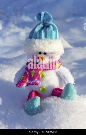 New year Christmas toy snowman in a blue cap sitting on the snow in a snowdrift close up Stock Photo