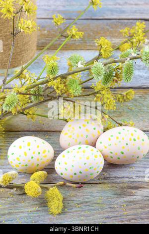 Easter composition of blooming willow twigs, dogwoods and Easter eggs with a pattern of yellow and green dots on a wooden retro background space close Stock Photo