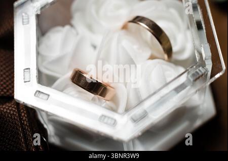 Close-up view of two gold wedding bands resting gently in a clear, geometric-shaped box lined with white tissue. The rings are smooth, shiny and symbo Stock Photo