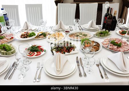 A beautifully arranged banquet table showcases a variety of cold cuts, salads, and appetizers. Elegant place settings and wine bottles complete the sc Stock Photo