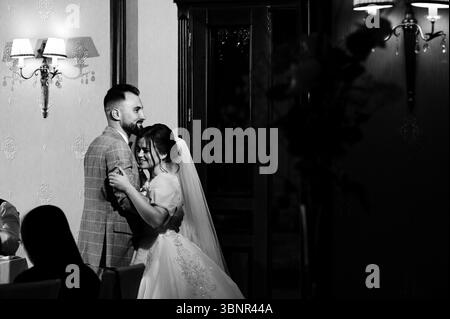 A black and white photograph of a bride and groom sharing a tender moment at their wedding reception. The couple is elegantly dressed, and the setting Stock Photo