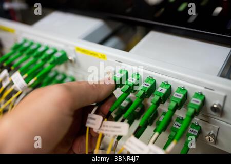 Technician hand is plugging green SC fiber connector into rack with yellow cables in flat design Stock Photo