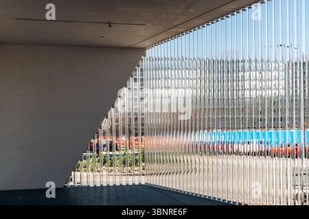 Milan, Italy - March 19, 2025 : Minimalist courtyard at Fondazione Prada with diagonal concrete wall and vertical glass fins reflecting the cityscape, Stock Photo