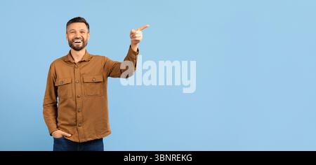 Happy young man pointing upward at copy space and laughing Stock Photo