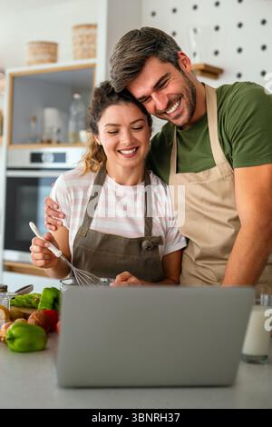Young couple using laptop computer to take part in online culinary workshop, cooking together Stock Photo