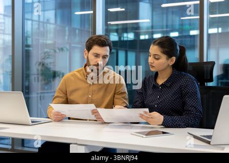A diverse team of colleagues collaborates in a modern office environment, reviewing documents and using technology during their work. Stock Photo