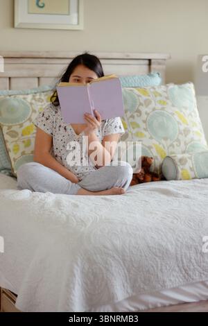 Young woman with down syndrome reading a book in bed Stock Photo