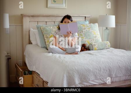 Young woman with down syndrome reading a book in bed Stock Photo