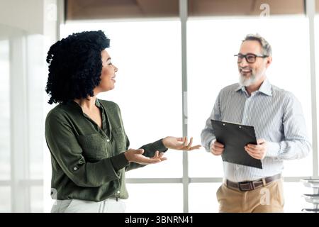 Two professionals engaging in collaborative discussion in office wearing corporate attire Stock Photo