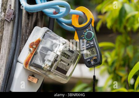 Digital clamp meter clamped on electric wire showing voltage reading on outdoor power system Stock Photo