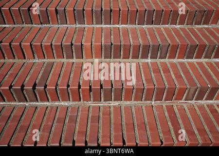 A close-up, straight-on view of stairs made from red brick. The repeating horizontal lines of the steps create a strong geometric pattern and a rich a Stock Photo