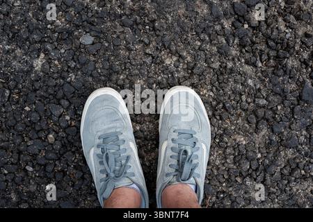 Top down view of classic casual sneakers on coarse, textures fresh asphalt background Stock Photo