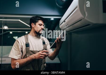 Technician performs maintenance on air conditioning unit while checking data on tablet Stock Photo