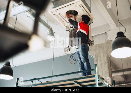 Technician performs installation work on ceiling-mounted air conditioning unit in modern office Stock Photo