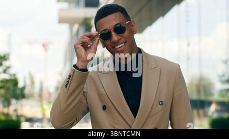 Smiling stylish fashionable confident African American business man posing in city outdoors wearing black sunglasses businessman guy male entrepreneur Stock Photo