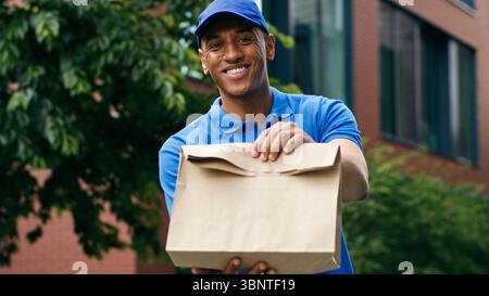 African American delivery food post service man courier in uniform in city worker deliver guy male hold delivered order meal shopping purchase package Stock Photo