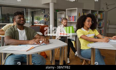 Four multiracial students studying learning education together in classroom high school university college writing in copybook lesson African man guy Stock Photo