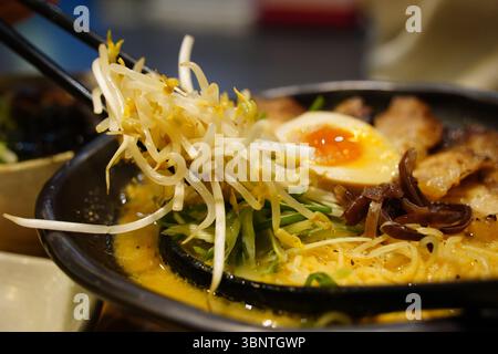 Close-up of Japanese Ramen Noodles with Chashu Pork, Soft-Boiled Egg, and Bean Sprouts in a Black Bowl Stock Photo