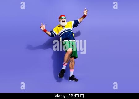 Elderly man performing energetic movements in colorful retro sportswear on vibrant background showcasing active lifestyle Stock Photo