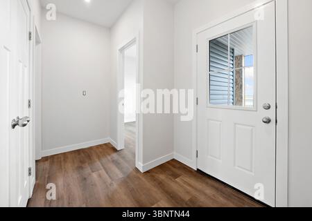 Hallway with a door leading to a room. The door is white and has a window. The hallway is empty and the door is closed Stock Photo
