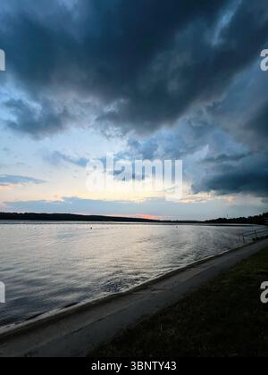 Dark clouds gather over the river as the light fades during evening Stock Photo