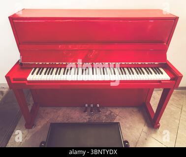 Front View of Red Upright Piano on Marble Floor Stock Photo