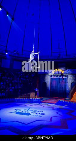Female aerialist performing on a suspended frame during a circus show in Batumi, Georgia. Strong theatrical blue lighting. Editorial use only. Stock Photo
