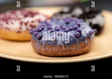 Donuts, macro shot. Three donuts are lying on a yellow plate. The focus is on a purple donut with glossy glaze and small round sprinkles. Stock Photo