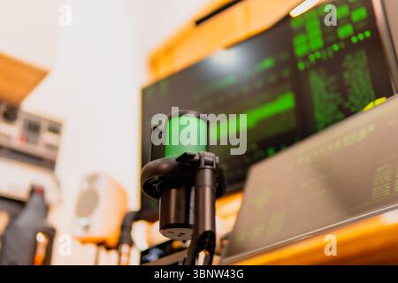 A close-up of a black microphone with green LED lighting, placed in front of multiple computer screens displaying hacker-style green codes and data. Stock Photo
