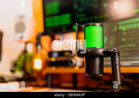 A close-up of a black microphone with green LED lighting, placed in front of multiple computer screens displaying hacker-style green codes and data. Stock Photo