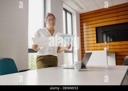 Businesswoman Carefully Analyzing Various Charts in a Contemporary Office Environment Stock Photo