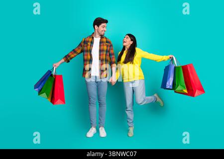 Young couple holding shopping bags and smiling, enjoying a joyful outing with colorful bags on a turquoise backdrop Stock Photo