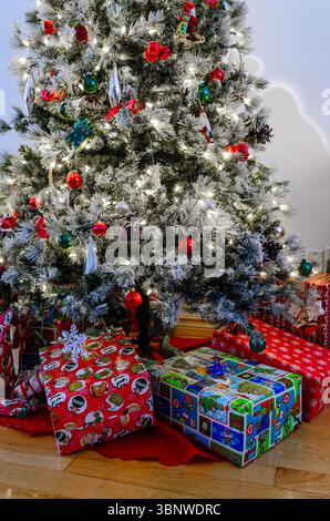 Decorated christmas tree on a hardwood floor with wrapped presents underneath against a white wall Stock Photo