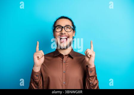 Cheerful Young Man Wearing Glasses Gesturing Excitedly Against Vibrant Blue Background in Stylish Fashion Stock Photo