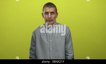Man in gray shirt displaying various nervous expressions against a vibrant yellow background, conveying emotion and intrigue. Stock Photo