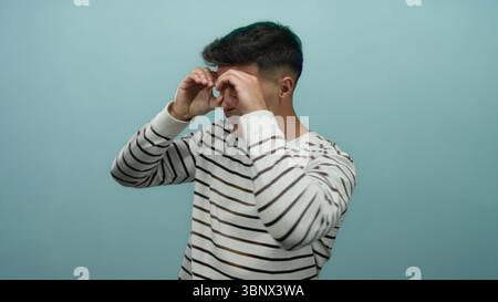 Young hispanic man in striped sweater posing against a blue background with a thoughtful expression, looking curious and focused with isolated setting Stock Photo