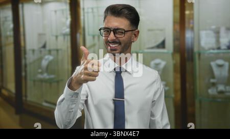 Man giving thumbs up in jewelry showcase building wearing shirt and tie with glasses and winking at camera; approval. Stock Photo