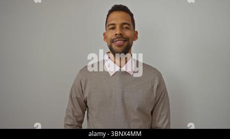 Young hispanic man standing isolated against a white background looking handsome and confident wearing a stylish sweater. Stock Photo